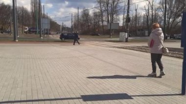 18-03-2023. Polonya, Sosnowiec. Avrupa şehrinin ölçülü yaşamı. Yetişkin bir kadın kaldırımda yürüyor ve güneşli bahar gününde tramvayı bekliyor. Şehir trafiğini izliyorum. Toplu taşıma programı.