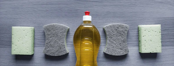 Banner with cleaning products.  Dish detergent and kitchen sponges on gray wooden table background. Concept of secrets and life hacks of housewife. Top view. Header for website, blog, article, cover.