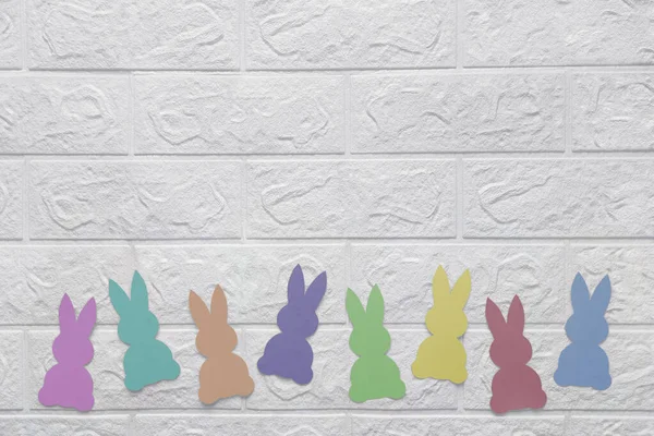 Kağıt tavşanlı beyaz duvar. Mesaj için yer. Beyaz tuğla duvara karşı renkli kağıtlardan kesilen tavşanlar. Uzayı kopyala Düz yatıyordu. Anaokulu, okul, çocuk mağazaları için şablon.