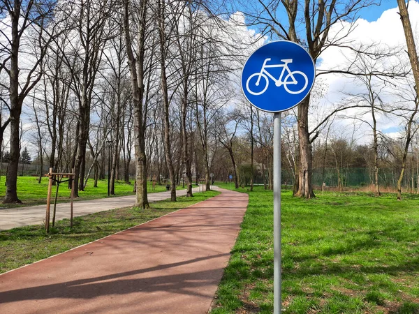 Bicycle lane sign indicating bike route. Bicycle path in spring park. Road sign is blue circle with white bicycle. Active lifestyle. Urban infrastructure for ecological transport and walks.