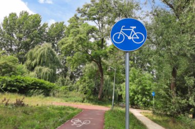 İşe bisikletle gidiyorum. Bisiklet yolu tabelası. Trafik levhası mavi daire üzerinde beyaz bisiklet, dağılmış yaz parkına, bisiklet yoluna ve patikaya karşı. Ekolojik taşımacılık için altyapı geliştirme kavramı.