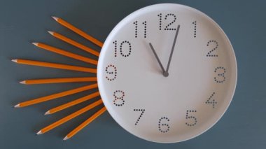 Saat 11 yönünde. Geri sayım başlasın. Çalışma zamanı. Okula dönelim. Saat ileri gidiyor. Mavi masa arkasında beyaz saat yüzlü, kurşun kalemli bir saat. Zaman ayarlı. Öğrenim anlayışı, son teslim tarihi, takvim.