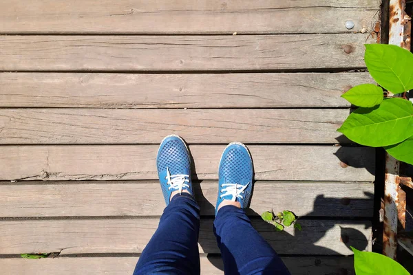 View from above on legs in moccasins on background of old wooden bridge. Women\'s feet in blue shoes and jeans stand on wooden plank road. Country walk on sunny day.