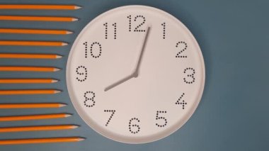 Saat ileri gidiyor. Mavi masa arkasında beyaz saat yüzlü, kurşun kalemli bir saat. Hiperlapse. Öğrenim anlayışı, son teslim tarihi, takvim.