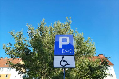 Ağaçların ve gökyüzünün arka planına karşı yol işareti. Erişilebilir park yeri kavramı. Engelli insanlar için uyarlanmış alanlar. İçerme.