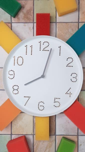 8時から クリーニングの時間 タイムラプス 8時以降の時計回りの手の動き タイル張りの壁に時計とカラフルなキッチンクリーニングスポンジ 日常の家事コンセプト — ストック動画