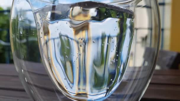 木制桌子上的一杯水 背景上的夏天绿油油的 阳光普照的景色 装有气泡水的双壁杯 — 图库视频影像
