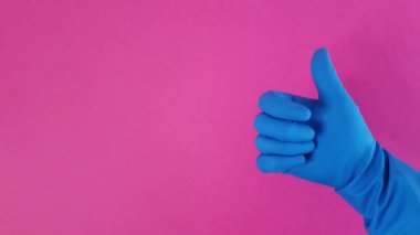 İyi niyet göstergesi. Mavi kauçuk eldivenli bir el, pembe bir arka plana başparmak kaldırır. Bu da iyi bir iş çıkardığını gösterir. Temizlik. Kopyalama alanı, reklam alanı, solda tasarım.