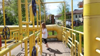Neşeli çocuk sarı borulardan oluşan labirentte yürüyor. Kahverengi saçlı, beyaz tişörtlü mutlu 10 yaşında bir kız. Çekicilik için çitlerden geçiyor. Lunapark efsanesi. Polonya Chorzow, 05-05-2023