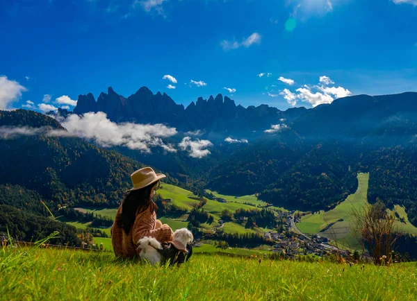 Dolomites Val di Funes, İtalya 'da saman şapkalı genç ve şık giyinmiş bir kız Alp çayırında dinleniyor. Santa Maddalena köyü manzarası ve çarpıcı resimlerin tadını çıkarıyordu. Ön plandaki adama odaklan..