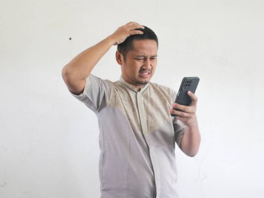 Adult Asian man showing confused expression when looking to his phone clipart