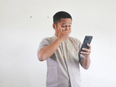 Adult Asian man showing shocked expression when looking to his phone clipart