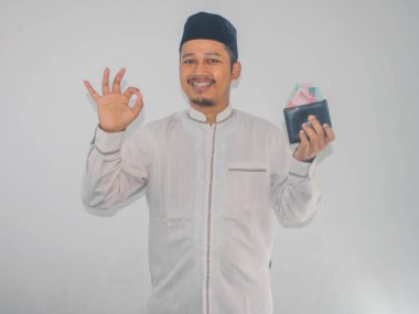 Adult muslim Asian man smiling and give OK finger sign while holding money clipart