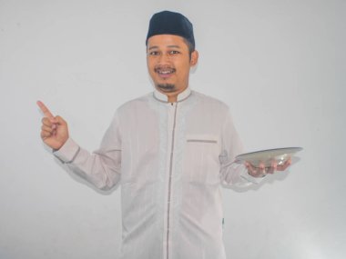 Müslüman Asyalı adam gülümsüyor ve elinde boş yemek tabağı tutarken sağ tarafı işaret ediyor.