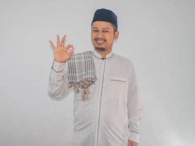 Moslem Asian man smiling happy and give OK finger sign at the camera clipart