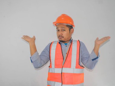 asian worker man wearing orange safety vest uniform and helmet clueless and confused expression with arms and hands raised. Doubt concept. clipart