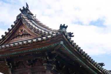 Bir Japon binasının çatısına tünemiş bir güvercini gösteriyor. Çatı koyu gri kiremitlerden yapılmıştır ve kıvrımlı saçakları ve sivri uçlu tepesi olan güzel bir tasarımı vardır..