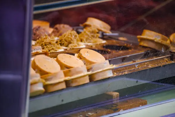 a vendor in the process of making hot and steaming wheel cakes