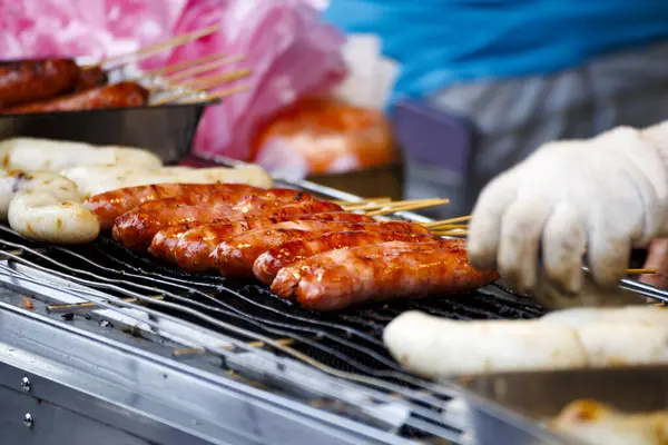 a person wearing gloves flipping sausages skewered on bamboo sticks on a grill