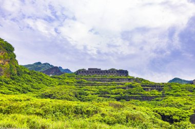 Yeşil bitki örtüsüyle kaplı bir yamaçta terk edilmiş birkaç bakır rafinerisinin kalıntıları arasında.