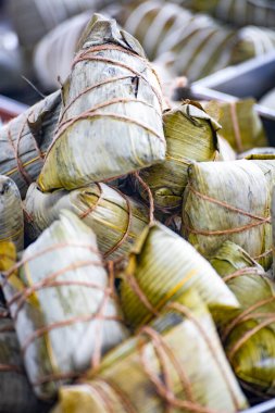 Bir kap bambu yapraklarına sarılmış ve iple bağlanmış geleneksel zongzi ile doludur.