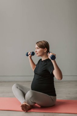 Spor giyimli, mutlu ve hamile bir kadın oturma odasında egzersiz yapıyor. Hamilelik sırasında doğum öncesi bakımı. Hamilelik süresince yaşam tarzı, sağlık ve spor kavramlarını. 