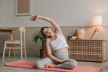 Hamile, evde yerde yoga yapıyor. Bekleyen genç anne yoga egzersizi yapıyor. Spor giyim sektöründe aktif ve mutlu bir kadın sabahları egzersiz yapıyor. Karnında esnek doğum öncesi anne.. 