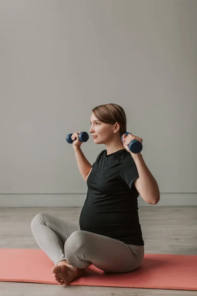 Happy young pregnant woman in sportswear doing exercises at home in the living room. Health Maternity prenatal care during pregnancy. Concept lifestyle, healthcare and sports during pregnancy.