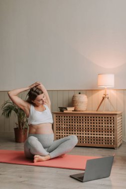 Genç bayan evde geriniyor. Genç bayan oturma odasında hamileliği sırasında egzersiz minderinde yoga yapıyor. Sağlıklı bekar anne online derste çalışıyor. Esneme, hamilelik yoga konsepti