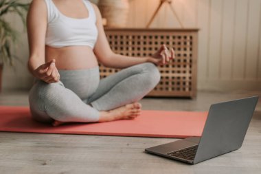 İnternette yoga yapan gülümseyen hamile bir kadın bilgisayara bakıyor. Hamilelik boyunca sağlıklı yaşam tarzı, sağlık ve spor kavramı. Yüksek kalite 4k görüntü