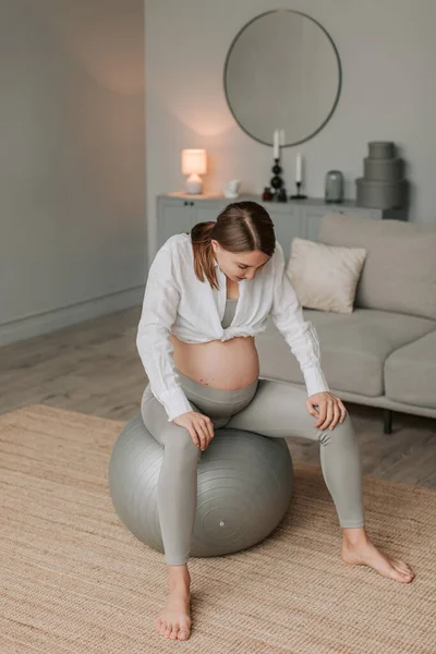 Young pregnant woman doing exercises and stretching sitting on fitball in living room at home. Fitness for pregnant women concept. Healthy pregnancy. 4K. High quality 4k footage