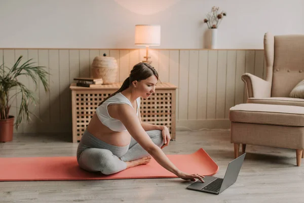 stock image Young smiling pregnant woman practicing yoga online looking on computer. Concept of healthy lifestyle, healthcare and sports during pregnancy. High quality 4k footage