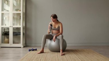 Genç, çekici, yorgun ve hamile bir kadın spor giyim bölümünde şişeden su içiyor. Yüksek kalite 4k görüntü