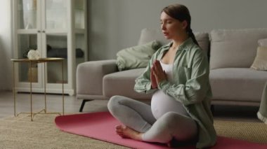 Sakin, hamile bir kadın temiz havayla derin bir nefes alıyor. Yoga lotusu evde rahat poz veriyor. Genç bir kadının hamileliği sağlıklı bir hayat için rahatlamak ve meditasyon yapmak. Yoga anneliği ve hamilelik sağlıklı. 