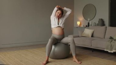 Egzersiz yapan ve esneme hareketleri yapan genç hamile bir kadın. Oturma odasında spor salonunda oturuyor. Hamile kadın konsepti için spor. Sağlıklı hamilelik. 4 bin. Yüksek kalite 4k görüntü