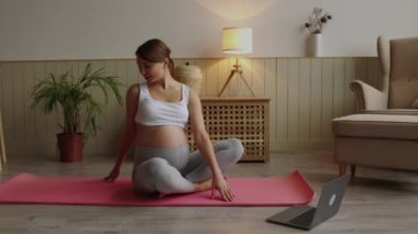 İnternette yoga yapan gülümseyen hamile bir kadın bilgisayara bakıyor. Hamilelik boyunca sağlıklı yaşam tarzı, sağlık ve spor kavramı. Yüksek kalite 4k görüntü
