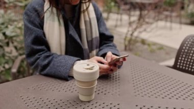 Kahve molası sırasında cep telefonuyla mesajlaşan ya da sörf yapan, çevre dostu, şehir merkezinde tekrar kullanılabilir bardakla gezen ya da atkı 4K eşarplı ceketli kadınları yakın plan çekimde çek. 