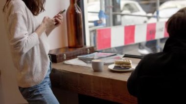 Akıllı telefon fotoğrafı kullanan mutlu güzel kadın blogcu ve kafe veya kahve dükkanındaki aboneleri için yemek videosu hazırlıyor. İçerik üreticisi cep telefonundan yaratıcı çekimler yaparak hikayeler üzerinde çalışıyor.