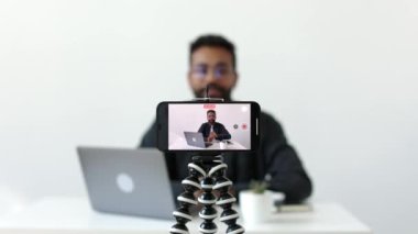 Kameralı telefona odaklan. Gözlüklü, Afro-Amerikan deneyimli bir adam internet kanalı için video bloğu kaydediyor. Ev yapımı stüdyo 4K 'deki beyaz masada oturuyor. Merhaba.