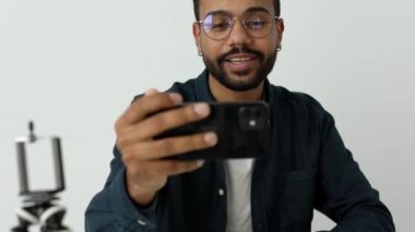 Gündelik donanma tişörtlü heyecanlı Amerikalı adam internet izleyicilerine canlı yayında gözlük takıyor. Genç adam etkileyici akış kayıt vlog ev yüksek kalite 4K görüntü