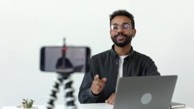Neşeli Afrikalı adam ev stüdyosunda video kaydediyor. Erkek kişi çevrimiçi konuşarak eğleniyor. Siyah gözlüklü, beyaz gözlüklü bir insan yüksek kalitede takipçilerle sohbet eder.