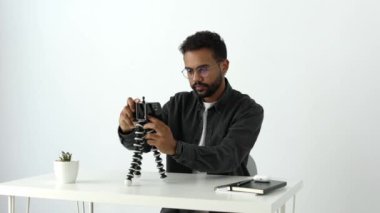 Gri tişörtlü, gözlüklü, siyah telefonlu, dokunmatik ekranlı, yakın çekim videolu çekici Afro-Amerikan bir adam masada oturuyor. Canlı, kamera çevrimiçi öğretmeye hazır.
