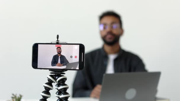 三脚に焦点を当てたカメラ電話で黒人男性の中出しし ノートパソコンで机に座って 居心地の良いスタジオオフィスでVlogを撮影しながらカメラで何かを説明高品質4K映像 — ストック動画