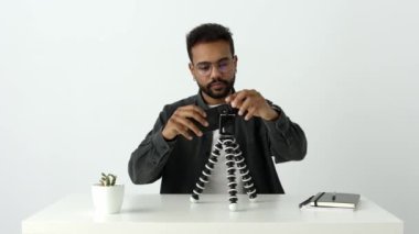 Gözlüklü yaratıcı Afrikalı erkek vlogger stüdyo içinde cihazlar hakkında konuşmak için tripoda telefon koyuyor. Yayın yoluyla takipçiler için yayına hazır olun. Yüksek kalite 4k görüntü