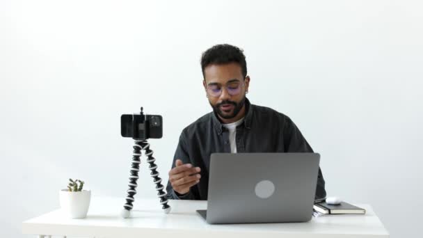 快乐英俊的黑皮肤小伙子 戴着眼镜 坐在白桌旁 带着笔记本和绿色 在线教育或远程工作 为互联网频道录制Vlog视频 商务会议4K — 图库视频影像