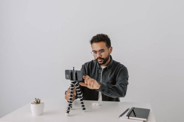 Neşeli, yakışıklı Afrikalı bir adam, gözlüklü bir etkilidir. Telefon kamerasını tripoda yerleştirip, sosyal ağlardaki takipçilere yeni kulaklık ya da cihaz sunumu hakkında video yayınlar.