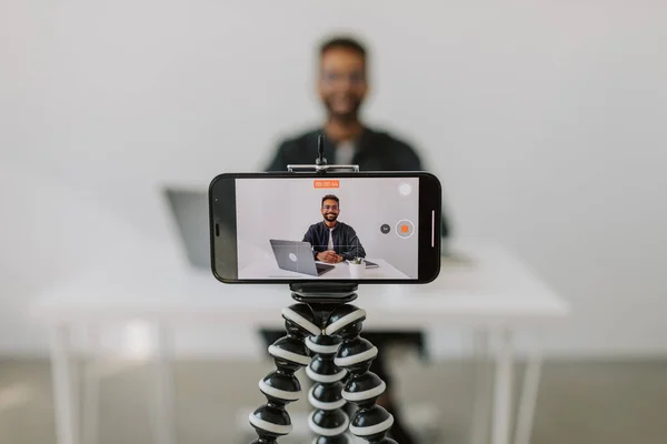 Head shot focused on phone camera with handsome young african ethnicity male applicant in glasses holding video call job interview with hr manager. Serious mixed race man coach looking at camera