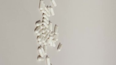 Vertical shot of white pills drop on grey or white surface with capsules. Medicine capsules on white background. High quality footage