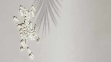 Vertical shot of white pills drop on grey or white surface with capsules. Medicine capsules on white background. High quality footage