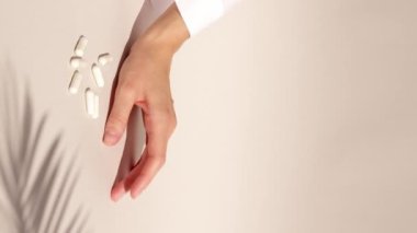 Hand with medical white capsules in moving shadow of windy fern bracken list on a beige background. High quality footage